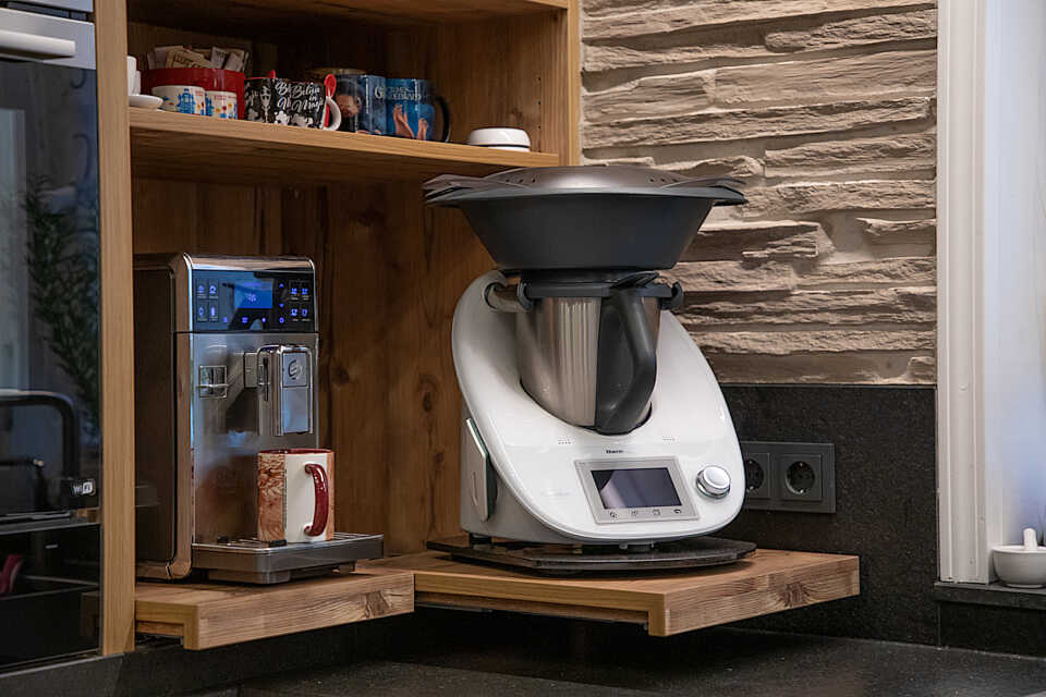 Offene Fächer. Im unteren Fach stehen Kaffeevollautomat und Thermomix auf ausziehbaren Böden, so dass beide gut verstaut werden können, man sie bei Bedarf aber herausziehen und so gut an sie herankommen kann.