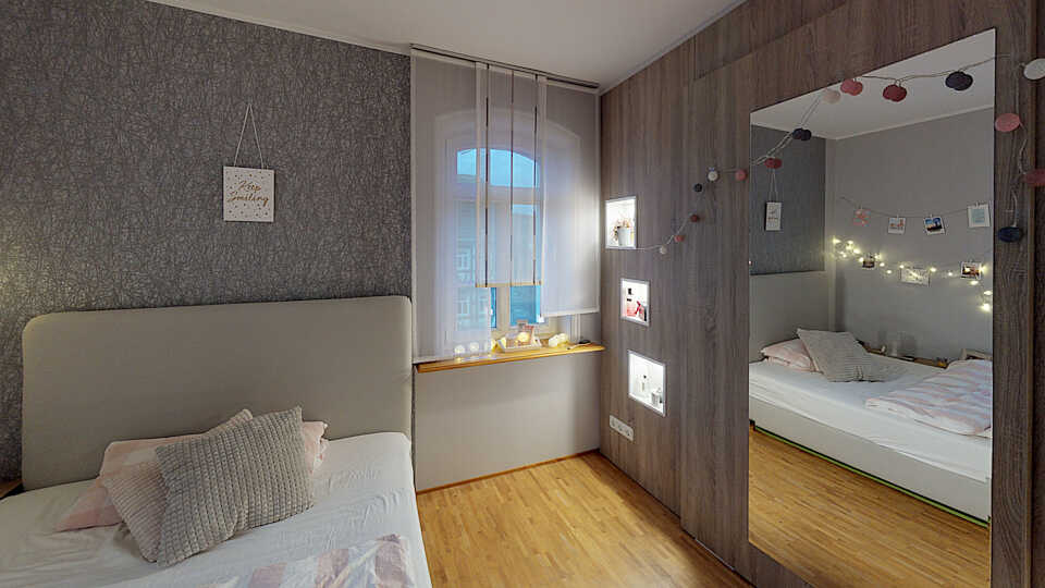 Schlafzimmerbereich mit Bett, Fenster, beleuchteten Wandnischen und Schiebetür mit großem Wandspiegel.